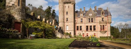 Een majestueus kasteel met stenen muren en hoge torens staat trots onder een blauwe lucht in het hart van Ierland. Omringd door weelderig groen gras en aangelegde tuinen, is dit historische juweeltje een must-see op elke rondreis door Ierland. Een charmant stenen pad draagt bij aan de betoverende aantrekkingskracht. | Echt Ierland Vakanties