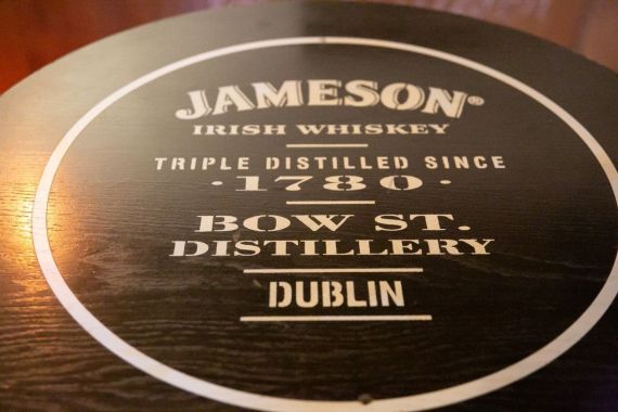 Op de bovenkant van een houten vat staat de witte tekst: "Jameson Irish Whiskey, Triple Distilled Since 1780, Bow St. Distillery, Dublin." Het gepolijste oppervlak en de zichtbare houtnerf roepen een klassieke, vintage charme op: een perfect aandenken aan uw urlaub Irland of rundreise Irland. | Echt Ierland Vakanties