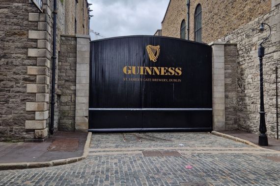 De grote zwarte poorten van het Guinness Storehouse in Dublin staan gesloten, met trots het woord "Guinness" en het harplogo. Omlijst door stenen gebouwen aan een charmante geplaveide straat, is het een must-see op elke rundreise in Ierland, zelfs onder een bewolkte hemel. | Echt Ierland Vakanties