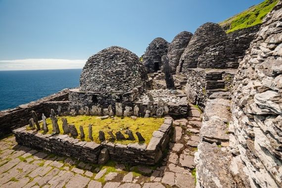 Oude stenen bijenkorfhutten op Skellig Michael, Ierland, gelegen op een rotsachtige helling met een helderblauwe lucht en de oceaan op de achtergrond. Stenen muren afgewisseld met grasvelden creëren een historische en ruige sfeer - een onvergetelijke stop voor elk Urlaub Irland-avontuur. | Echt Ierland Vakanties