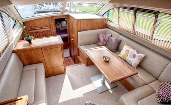 Het interieur van de hut op deze dromerige "vakantie Ierland"-ontsnapping beschikt over L-vormige beige banken versierd met decoratieve kussens rond een houten tafel. Een kleine houten kast met een potplant staat tegen de muur, terwijl grote ramen met jaloezieën natuurlijk licht binnenlaten en de gezellige vloerbedekking verlichten. | Echt Ierland Vakanties