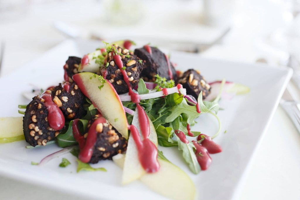 Een gastronomische salade op een vierkant wit bord siert de elegante eetzaal van het Witte Huis. Met in plakjes gesneden gekookte bieten met bessendressing, dunne plakjes groene appel, rode ui, gemengde sla en bestrooide noten, is het kunstig versierd met kruiden in een heldere, minimalistische setting. | Echt Ierland Vakanties