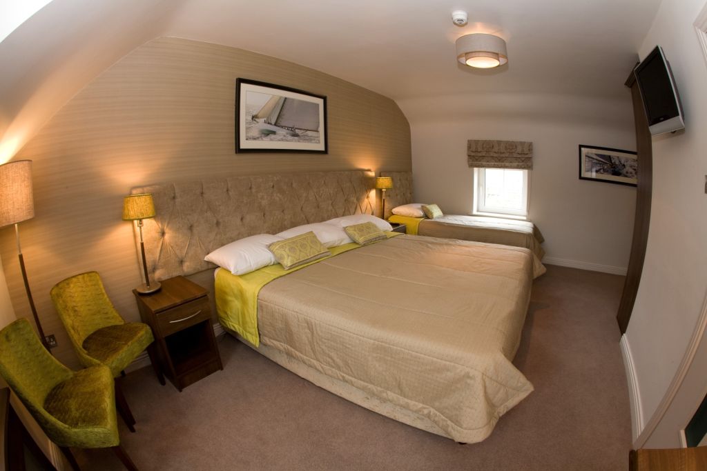 Het Hotel Granville beschikt over een kamer met twee bedden, gekleed in beige spreien geaccentueerd door verfrissend limoengroen. Een gewatteerd hoofdeinde verenigt de ruimte, terwijl een houten nachtkastje met een lamp tussen de bedden staat. De kamer heeft een raam versierd met patroontinten en ingelijste kunst, waaronder pluche tapijt en een aan de muur gemonteerde tv ligt. | Echt Ierland Vakanties