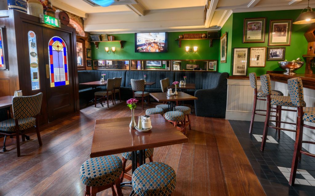 Het gezellige pubinterieur van het Granville Hotel heeft een houten vloer, groene muren en een mix van zitplekken en barzitplaatsen. Tafels versierd met kleine bloemenvaasjes staan onder een gemonteerde tv, terwijl ingelijste decoratie en een glas-in-looddeur bij de zitplekken een warme en uitnodigende sfeer creëren. | Echt Ierland Vakanties