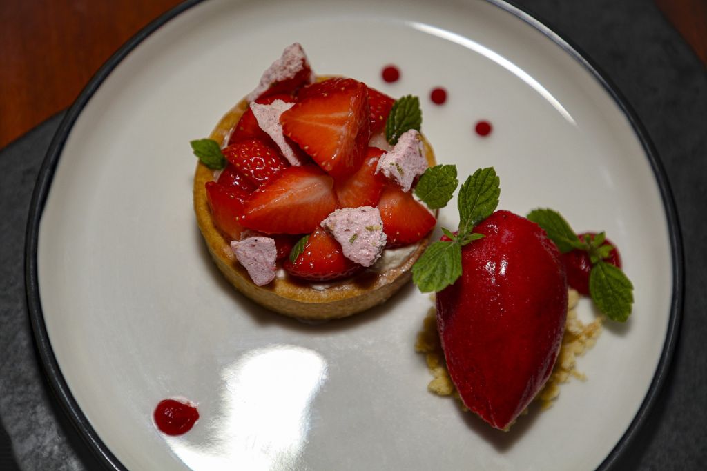 Een dessertbord met een taartje, bedekt met verse aardbeien, kleine stukjes roze meringue en muntblaadjes. Naast het taartje ligt een gladde bol rode sorbet, gegarneerd met munt en stipjes rode saus op het witte bordje. | Echt Ierland Vakanties