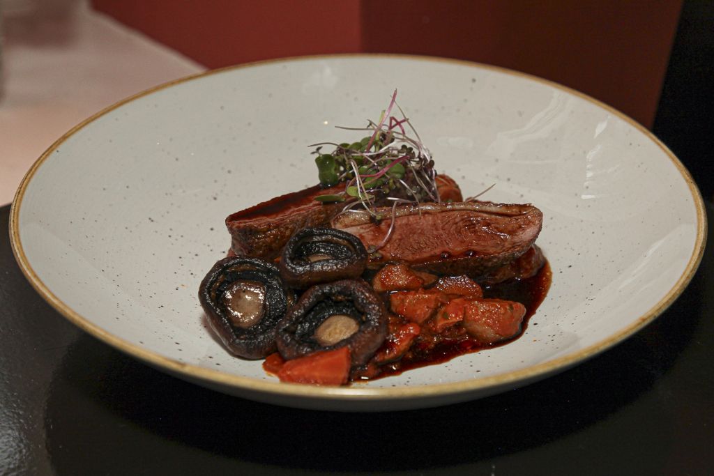 Een witte kom bevat gebakken plakjes eendenborst, geglazuurde champignons, blokjes wortel in een donkere saus en een garnering van microgroenten, alles kunstig gerangschikt tegen een donkere achtergrond. | Echt Ierland Vakanties