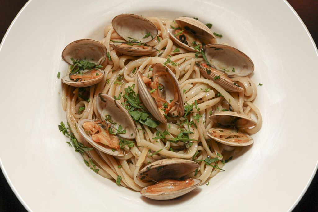 Een witte kom gevuld met linguinepasta, bedekt met open venusschelpen en gehakte peterselie. De pasta is licht bedekt met saus en de venusschelpen zijn gelijkmatig verdeeld, wat zorgt voor een frisse en smakelijke presentatie van de zeevruchten. | Echt Ierland Vakanties