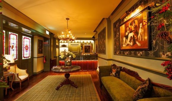 Elegante hotellobby met warme verlichting, glas-in-looddeuren, een sierlijke kroonluchter, een groenfluwelen bank, bloemstukken en klassieke schilderijen op muren met motieven. Een balie met houten lambrisering en een groot vloerkleed maken de gezellige, vintage sfeer compleet. | Echt Ierland Vakanties