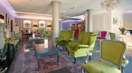 Een stijlvolle lounge in het Hillyard House Hotel in Castlewellan heeft groenfluwelen fauteuils, paarse stoelen, kroonluchters en een open haard. Zuilen, een trap met rode vloerbedekking, moderne kunst en zachtpaarse verlichting creëren een chique, uitnodigende sfeer. | Echt Ierland Vakanties