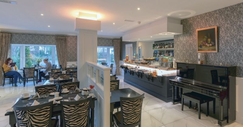 Een stijlvol restaurant in het Hillyard House Hotel, Castlewellan, met stoelen met zebrapatroon, een zwarte piano en een buffetbalie. Gasten genieten van grote ramen met uitzicht op de buitenlucht te midden van een elegante inrichting en ingelijste kunst. | Echt Ierland Vakanties